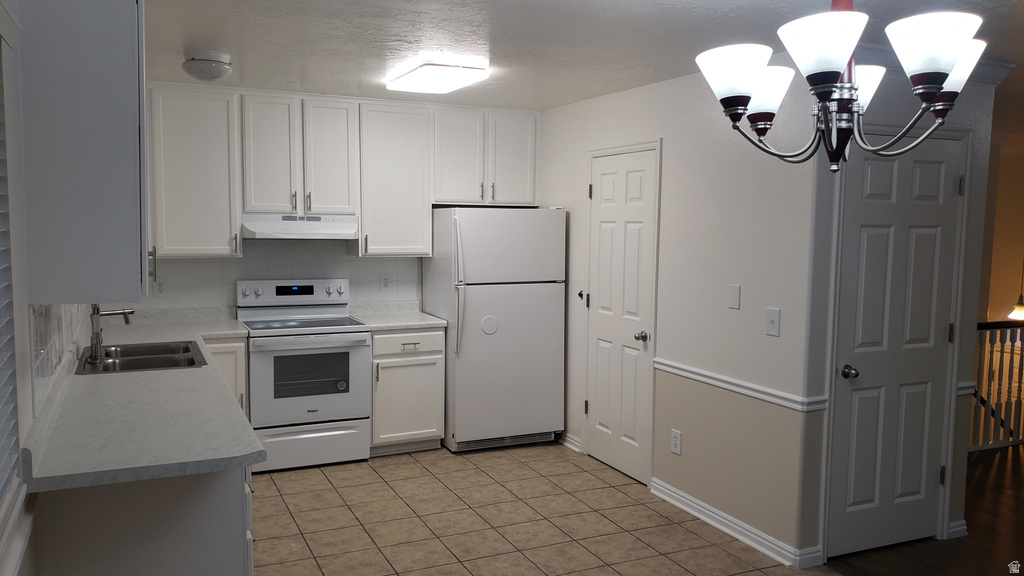 Kitchen with white appliances, a chandelier, light countertops, hanging light fixtures, and white cabinetry