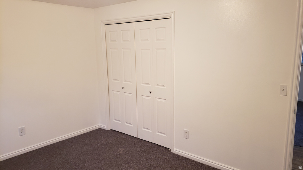 Unfurnished bedroom with dark carpet and a closet