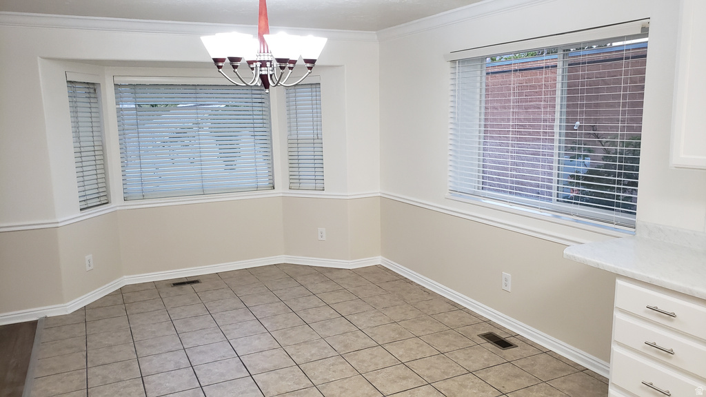 Unfurnished dining area with light tile patterned flooring, a chandelier, and ornamental molding