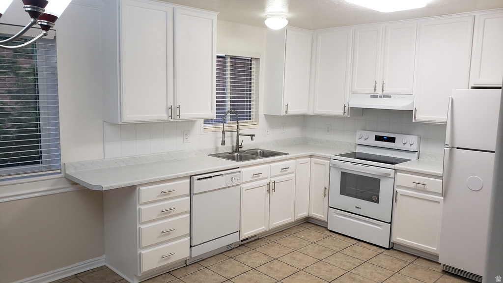 Kitchen with white appliances, light countertops, white cabinets, under cabinet range hood, and light tile patterned floors
