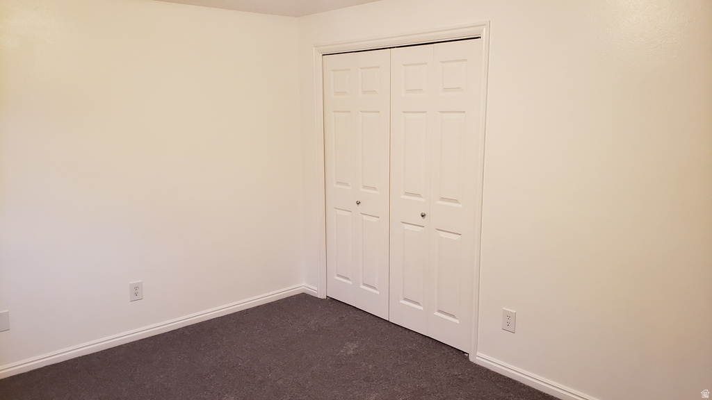 Unfurnished bedroom featuring dark carpet and a closet