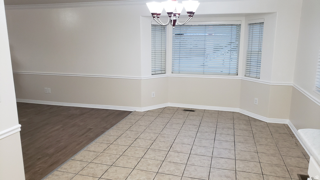 Unfurnished dining area featuring light tile patterned flooring, a chandelier, and crown molding