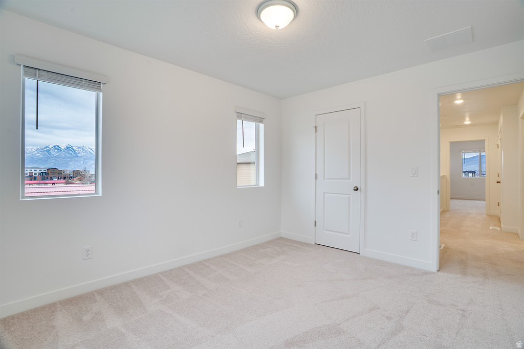 Unfurnished bedroom with light carpet and multiple windows