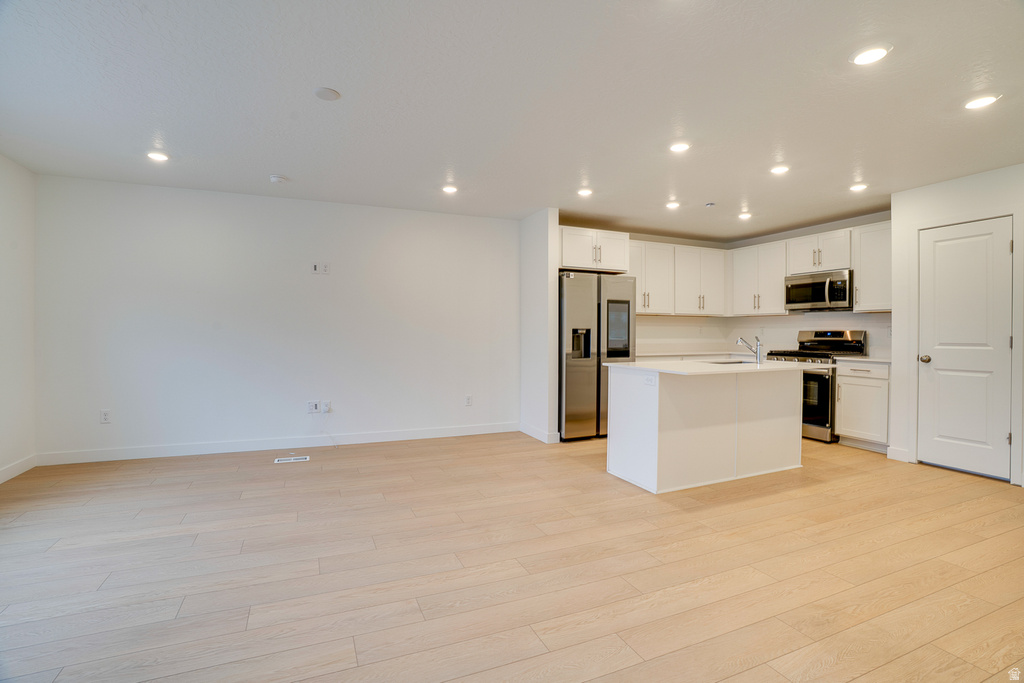 Kitchen with an island with sink, open floor plan, white cabinets, appliances with stainless steel finishes, and light wood-type flooring