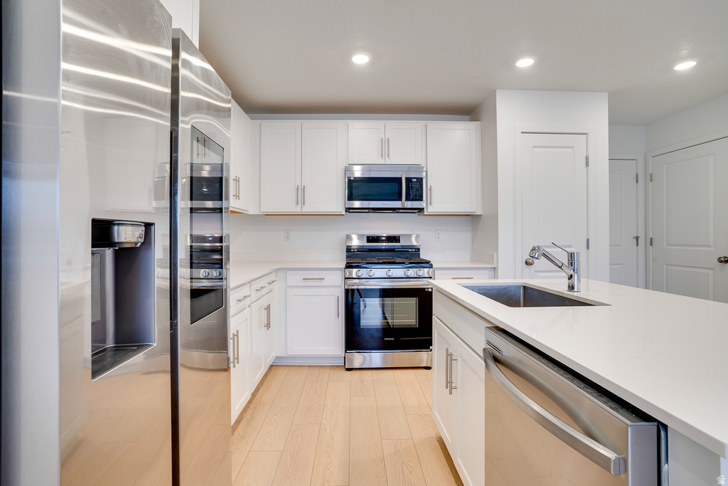 Kitchen with stainless steel appliances, white cabinets, recessed lighting, light stone counters, and light wood finished floors