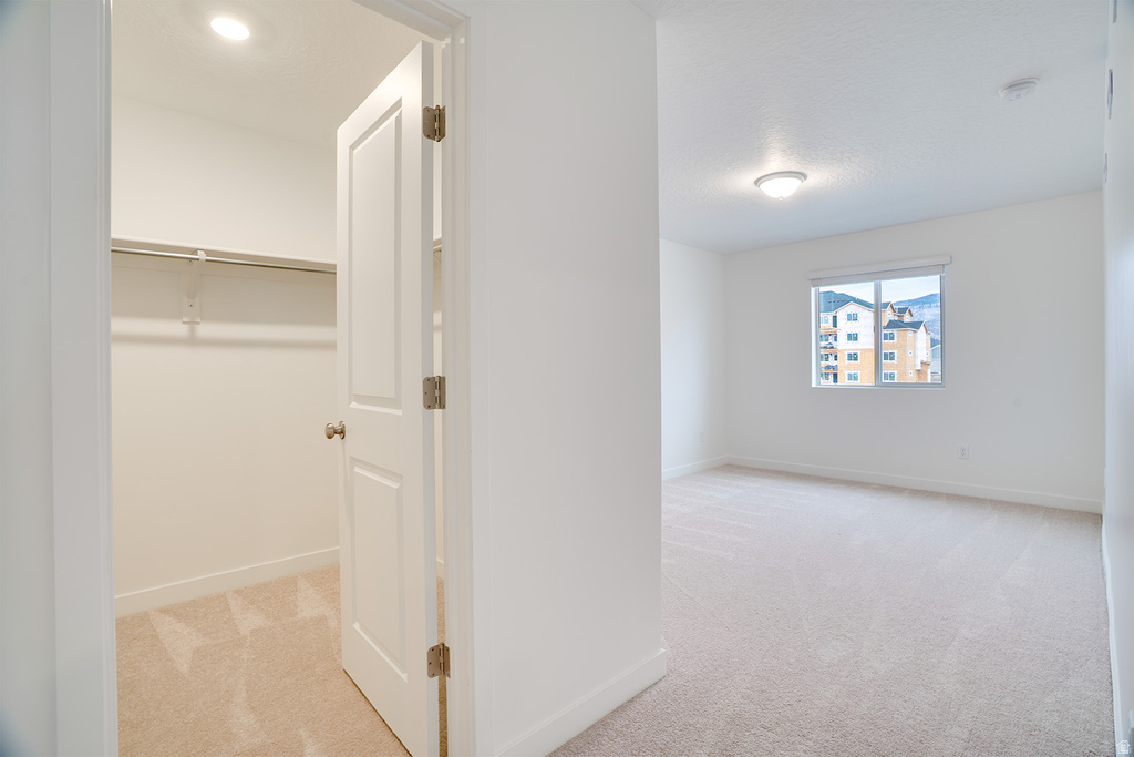 Hallway with light colored carpet and a textured ceiling