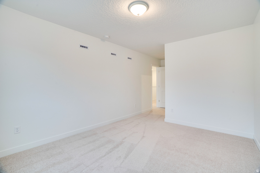 Empty room featuring a textured ceiling and light colored carpet