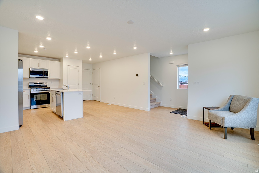 Kitchen featuring appliances with stainless steel finishes, white cabinets, a center island with sink, open floor plan, and recessed lighting