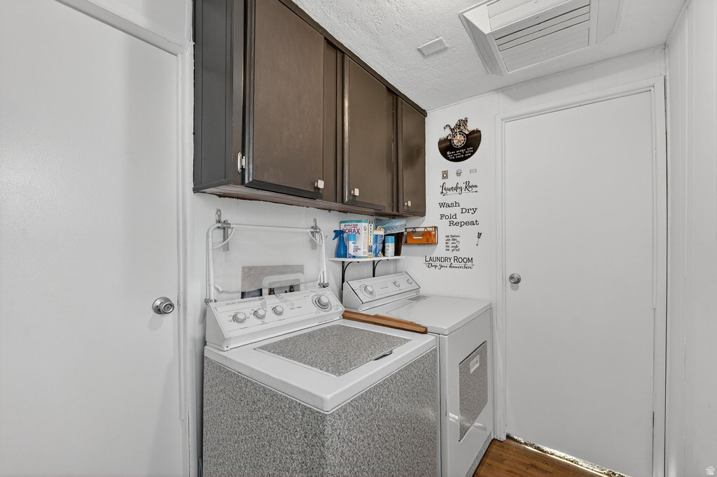 Laundry room with cabinet space, washer and dryer, a textured ceiling, and wood finished floors