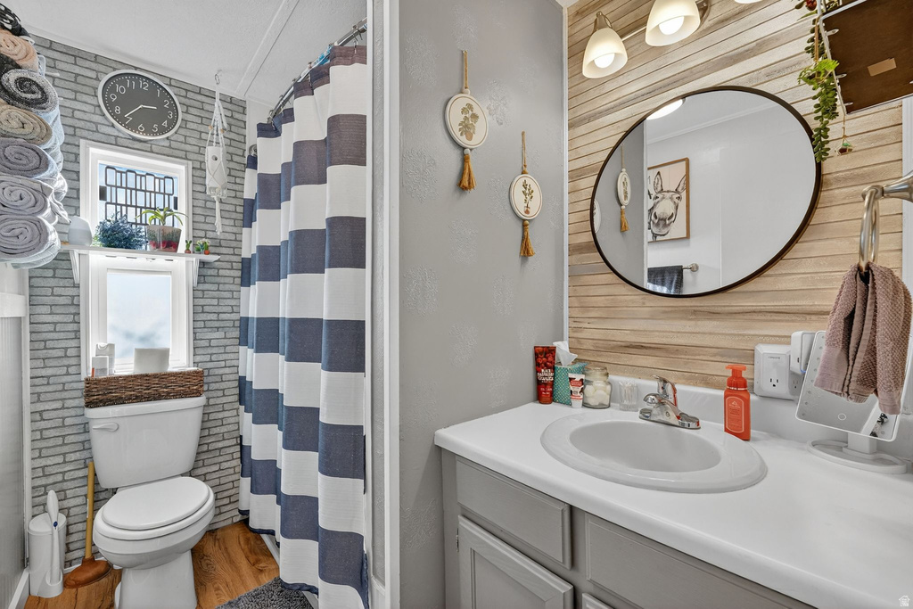 Full bathroom with vanity, a stall shower, wood walls, light wood-style flooring, and brick wall
