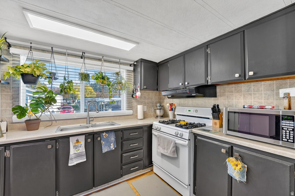 Kitchen featuring dark cabinets, white gas range, stainless steel microwave, light countertops, and decorative backsplash