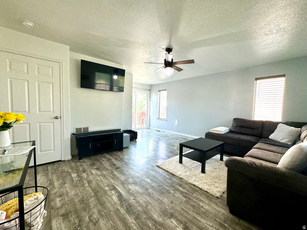 Living area with a textured ceiling, dark wood-style flooring, and ceiling fan
