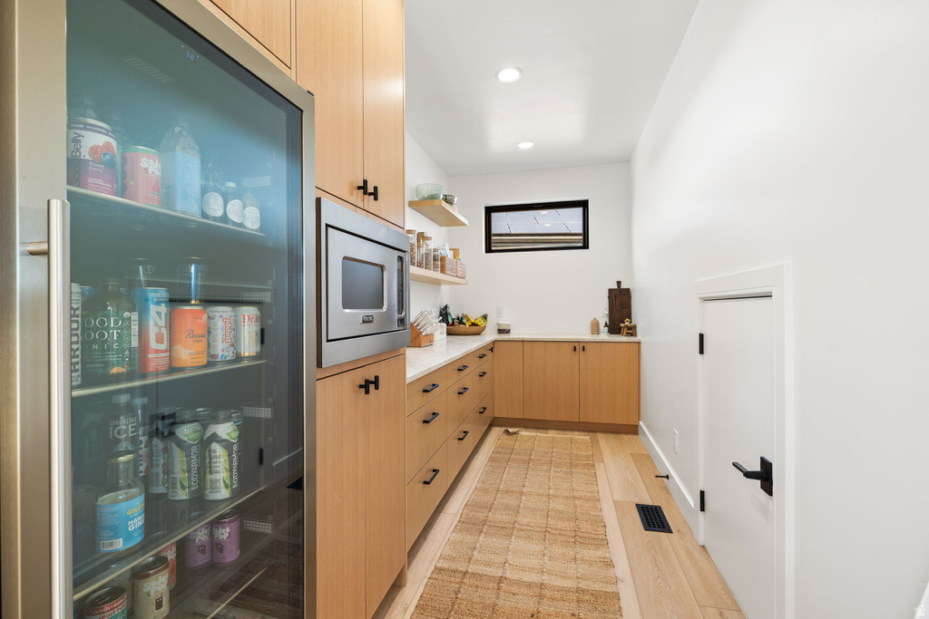 Kitchen featuring light brown cabinets, stainless steel microwave, open shelves, light wood-style flooring, and recessed lighting