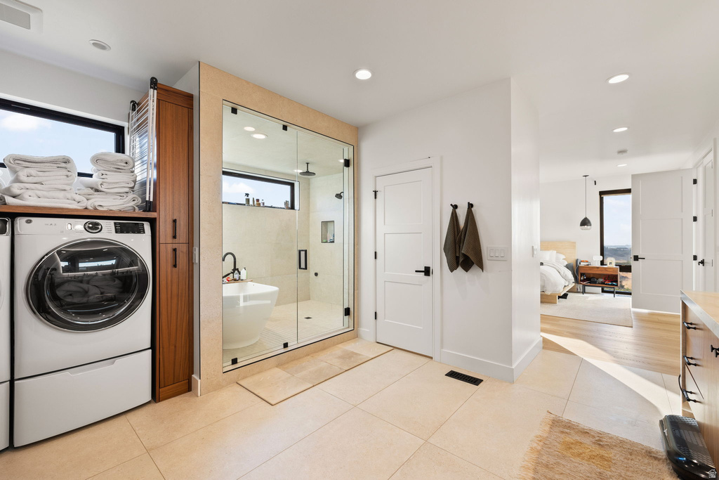 Full bath with ensuite bath, a shower stall, a freestanding tub, light tile patterned flooring, and washing machine and dryer
