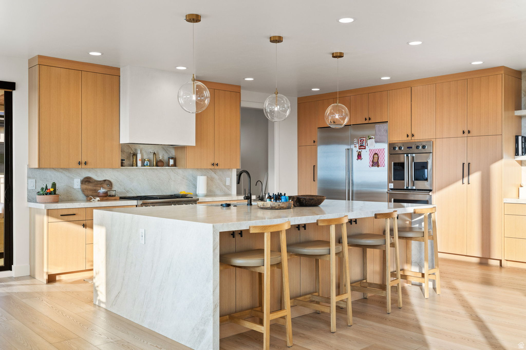 Kitchen featuring stainless steel appliances, open shelves, hanging light fixtures, a kitchen bar, and light stone counters