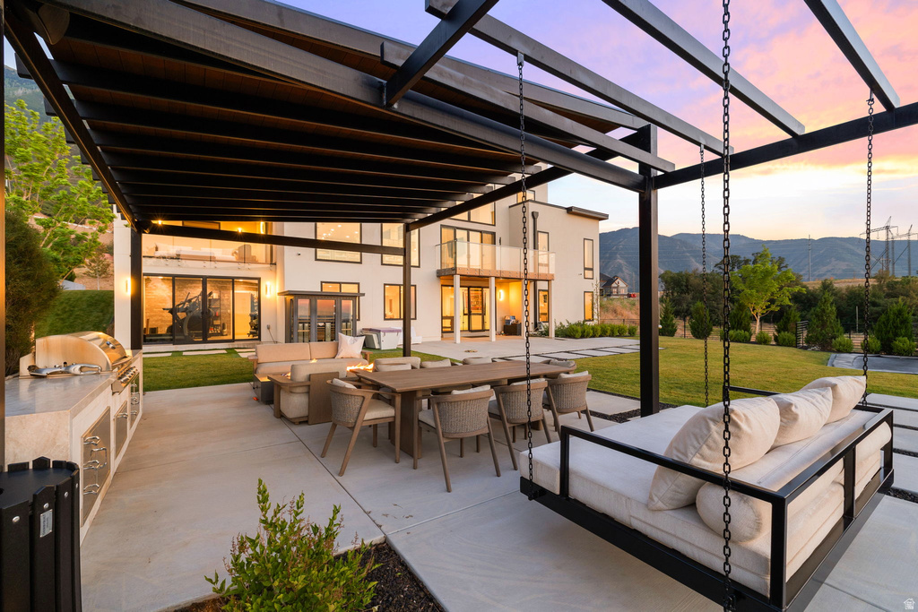 Patio terrace at dusk featuring outdoor dining area, outdoor lounge area, exterior kitchen, and a lawn