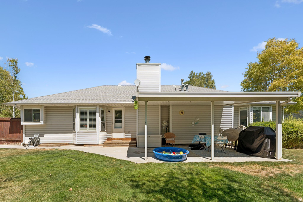 Back of property featuring a patio area, a lawn, roof with shingles, and a chimney