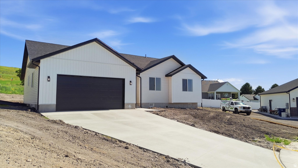 Contemporary residence featuring white vertical siding, dark trim accents, a black garage door, and a concrete driveway
