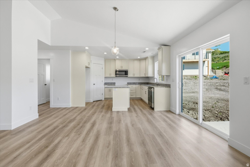 Open-concept living space featuring wood-finish flooring, vaulted ceilings, a kitchen island, stainless steel appliances, and a sliding glass door