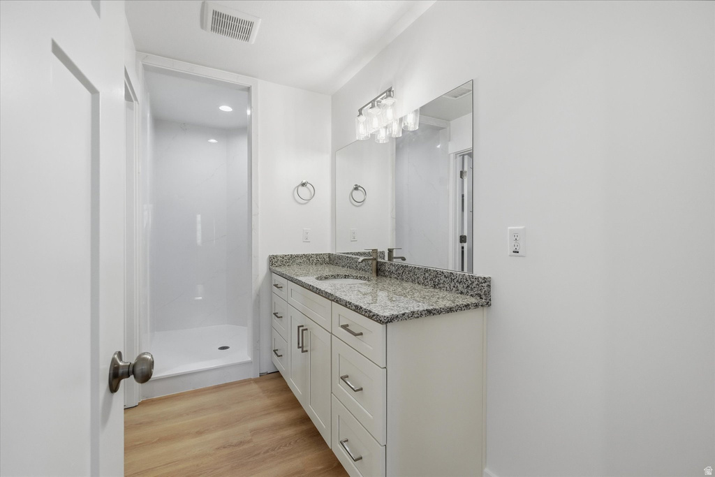 Contemporary bathroom featuring a spacious white shower stall, a vanity with ample storage, a speckled countertop, a rectangular mirror, and wood-finish flooring