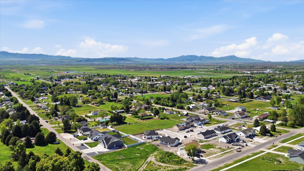 Expansive aerial photography showcasing a residential neighborhood with surrounding green fields and distant mountains under a clear sky