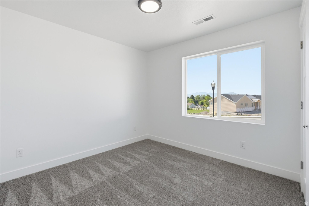 Spacious room featuring neutral carpeting, white walls, a large window, a modern ceiling light fixture, and white trim