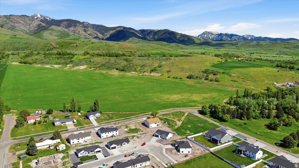 Residential properties situated on paved streets, bordered by expansive green fields and distant mountains with snow-capped peaks