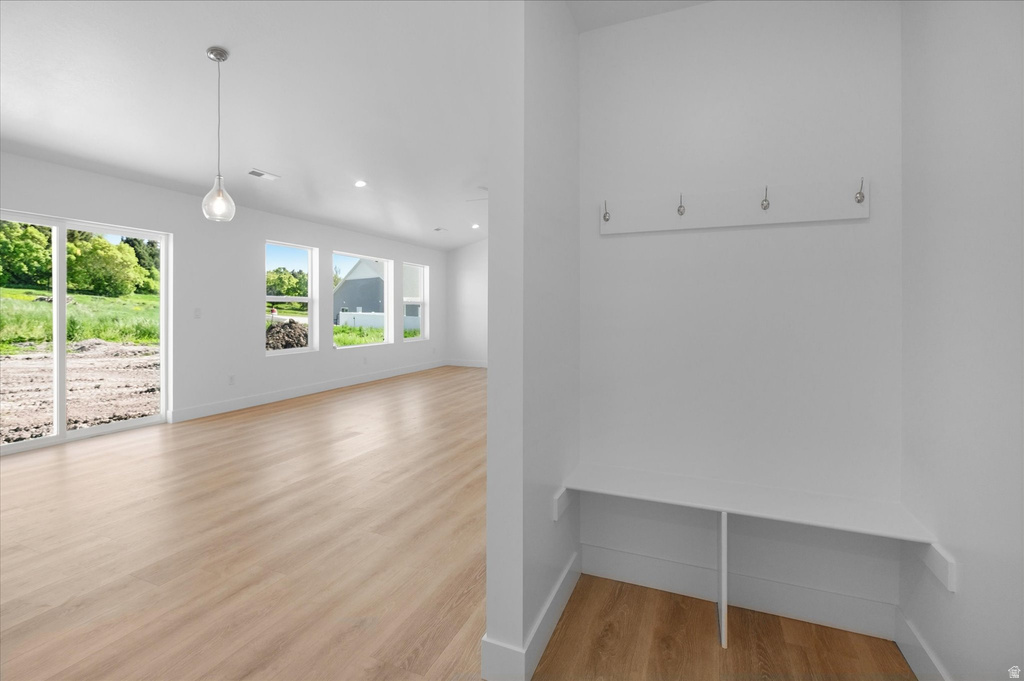 Open-concept living space with light wood-finish flooring, a contemporary pendant light fixture, recessed lighting, and multiple windows