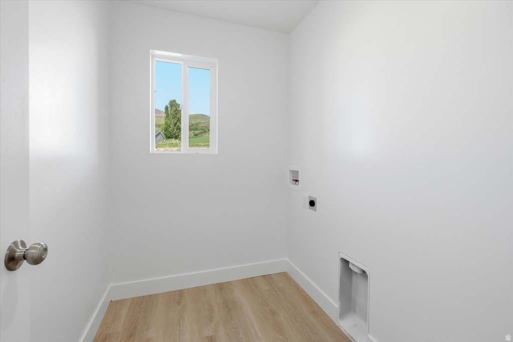 Utility room featuring a window with a mountain backdrop, wood-finish flooring, and white walls with baseboards