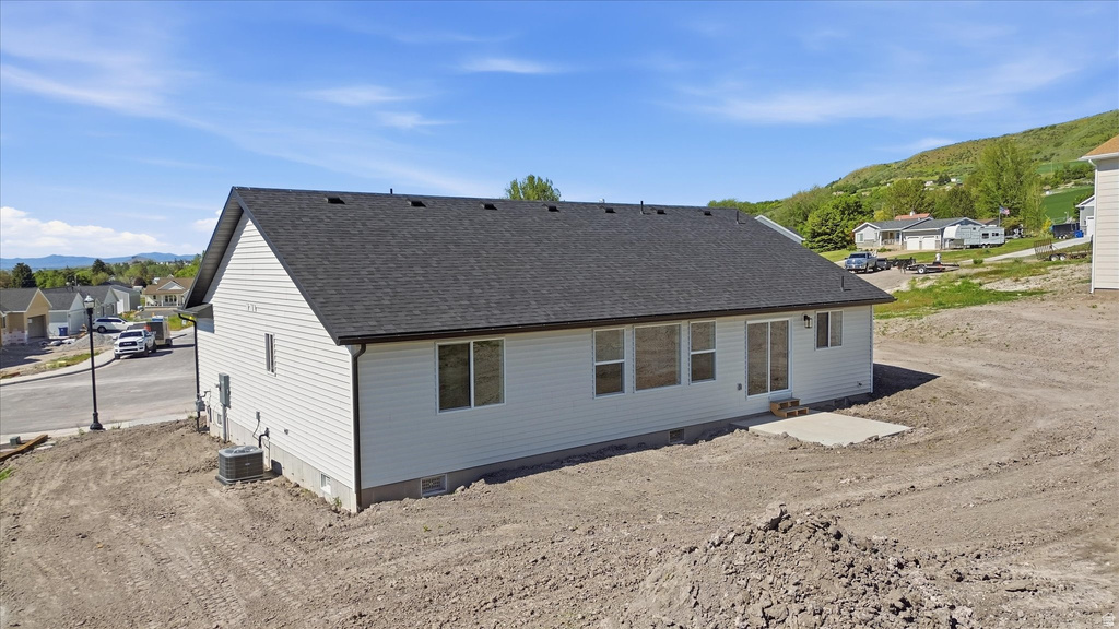 Contemporary residence featuring a dark shingle roof, light-toned siding, and a concrete patio