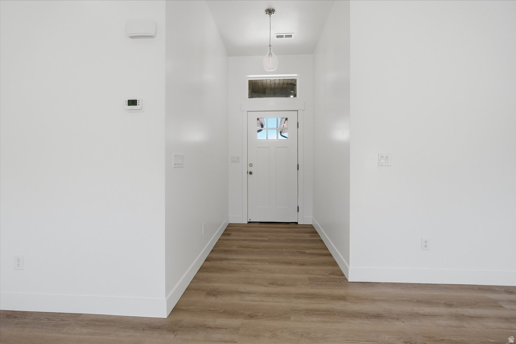 Foyer featuring light wood-finish flooring, crisp white walls, and a recessed panel front door with transom window