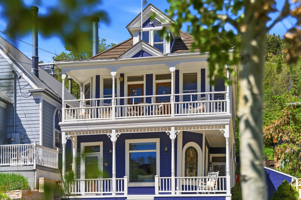 Victorian-style residence featuring a prominent blue facade, white trim, and a multi-level porch with ornate railings