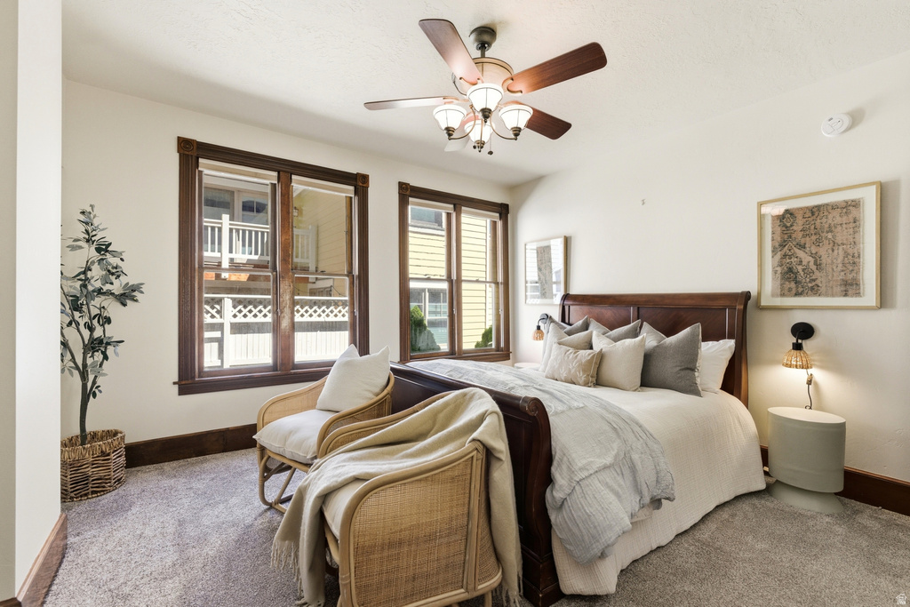 Carpeted room featuring a ceiling fan with integrated lighting, dark wood trim around windows and baseboards, and a bed with a dark wood headboard