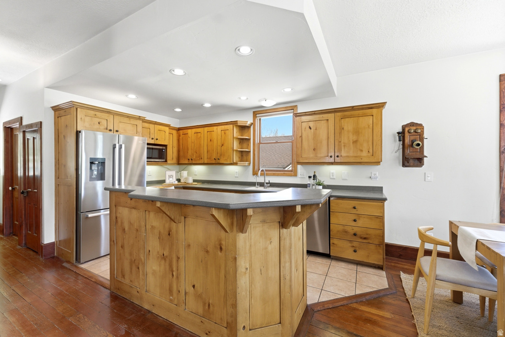 Kitchen featuring light wood cabinetry, stainless steel appliances, a central island with countertop seating, and recessed lighting