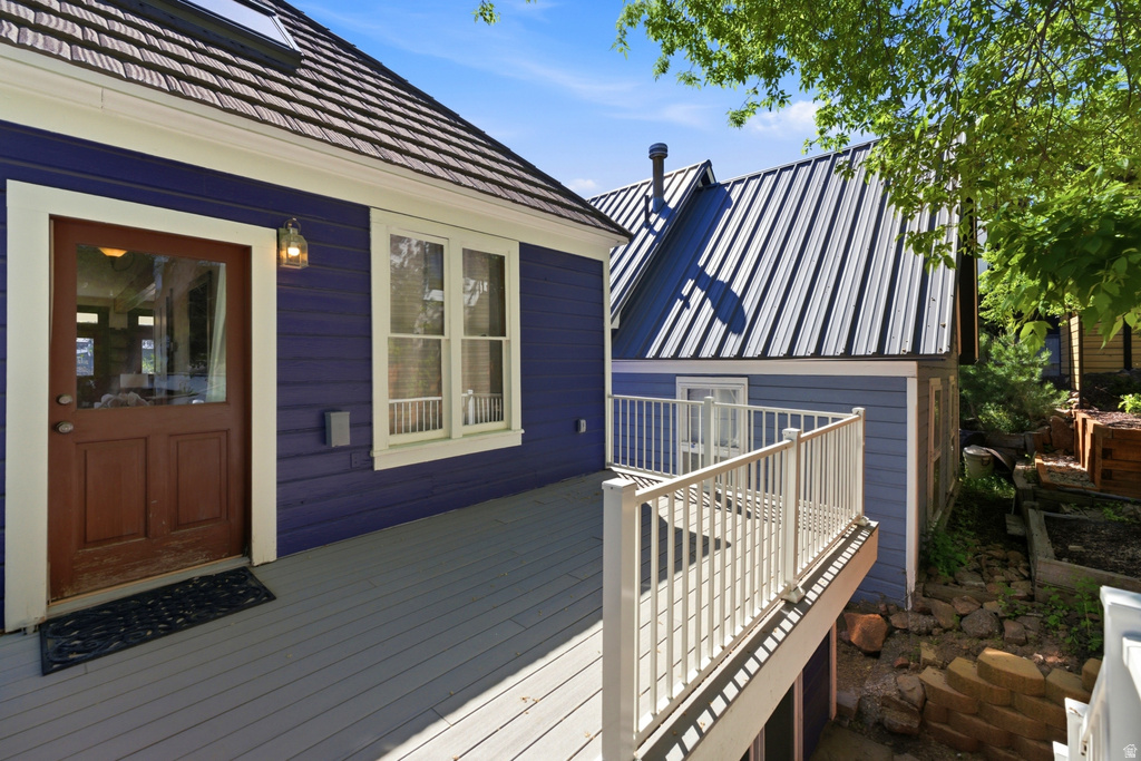 Exterior deck with a wood-finish floor, white railing, and a brown entry door with a glass pane