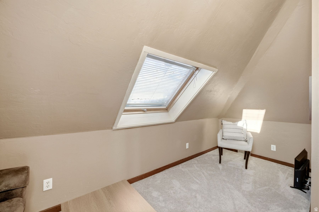 Sloped ceiling room featuring an operable skylight with integrated blinds, light gray carpet flooring, and a baseboard trim