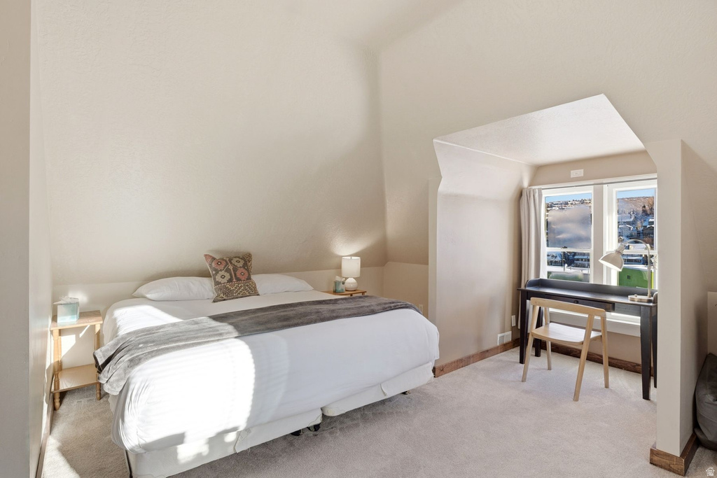Carpeted bedroom with sloped ceilings, recessed window area, and neutral wall tones