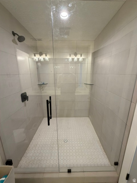Contemporary walk-in shower featuring a frameless glass enclosure, matte black fixtures, white subway tile walls, and a white hexagonal tile floor