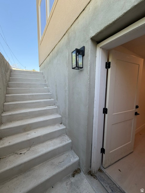 Concrete exterior stairs ascending alongside a stucco-finished wall, featuring a black-framed outdoor light fixture and a white paneled door with black hardware