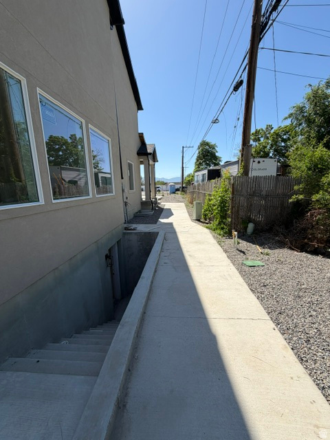 Concrete walkway alongside a stucco exterior featuring multiple windows, a basement entrance with concrete steps, and a gravel perimeter