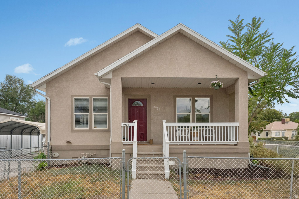 View of front of property with a gate, a porch, stucco siding, a fenced front yard, and a detached carport
