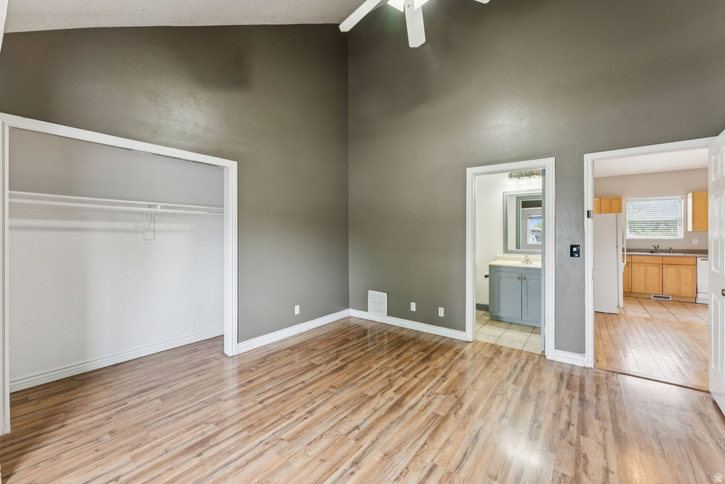 Unfurnished bedroom featuring freestanding refrigerator, a closet, light wood-style floors, ceiling fan, and a high ceiling