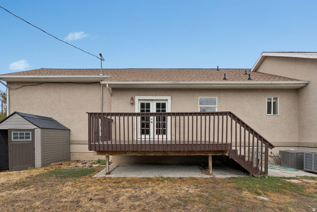 Rear view of property with a wooden deck, a storage unit, stucco siding, and a shingled roof