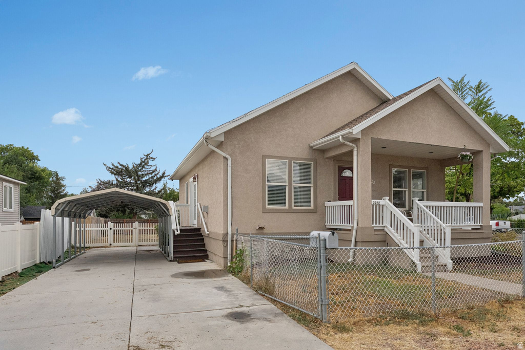 View of front facade featuring stucco siding, a detached carport, a gate, driveway, and a porch