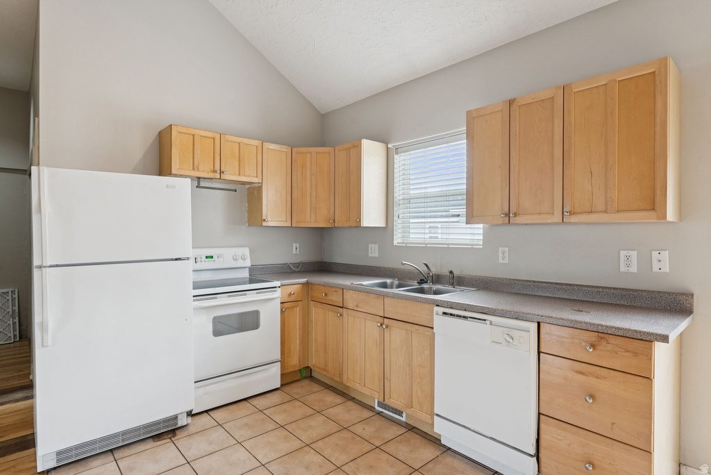 Kitchen with light wood finish cabinets, white appliances, vaulted ceiling, light countertops, and light tile patterned floors