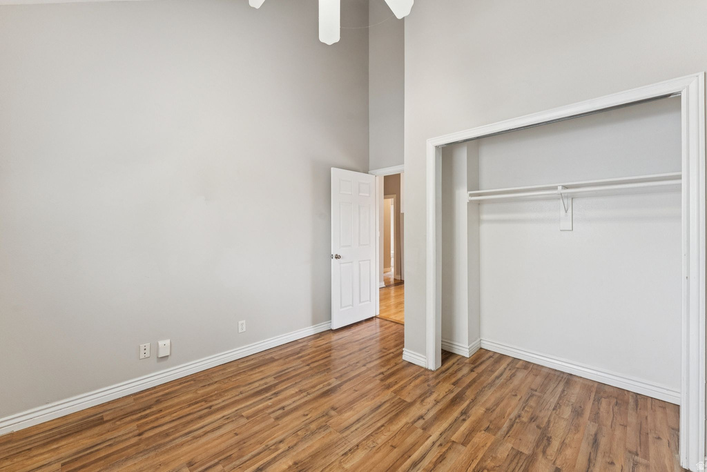 Unfurnished bedroom with a high ceiling, wood finished floors, a closet, and a ceiling fan