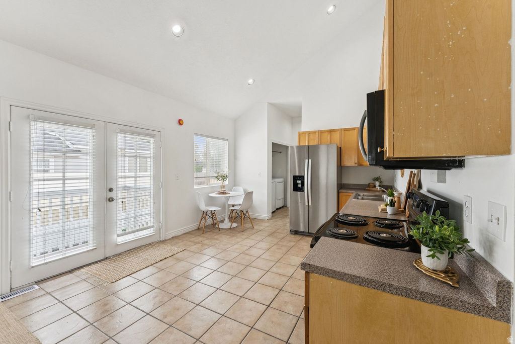 Kitchen featuring dark countertops, french doors, black appliances, lofted ceiling, and light tile patterned flooring