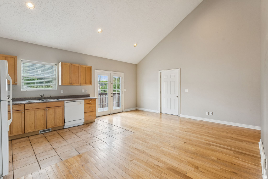 Kitchen with light wood-style flooring, dark countertops, white appliances, recessed lighting, and vaulted ceiling