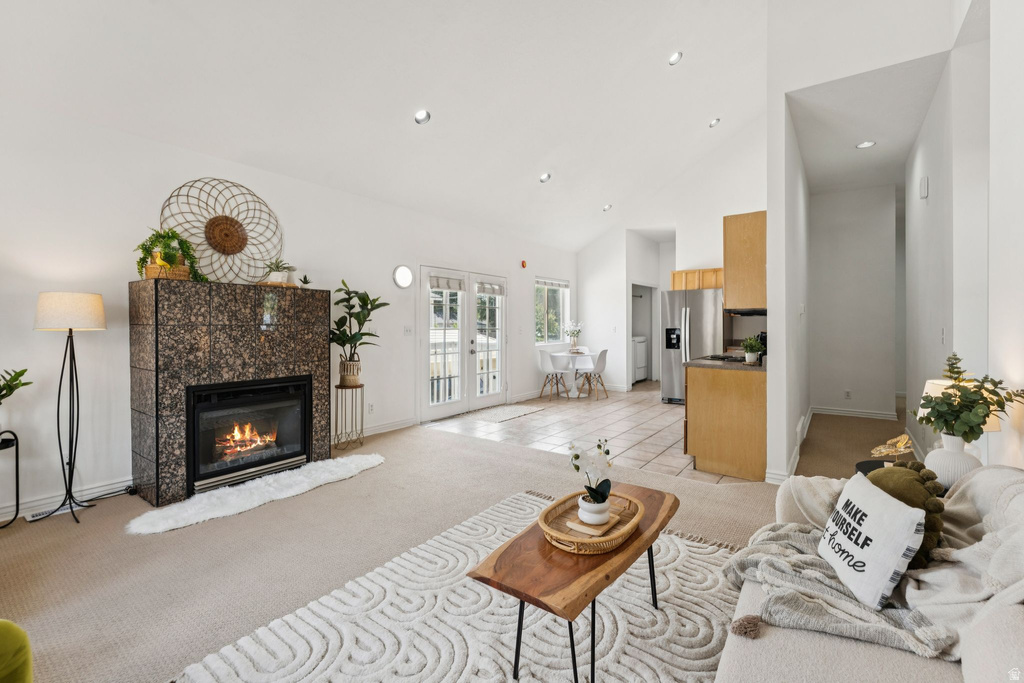 Living room featuring light colored carpet, a tiled fireplace, lofted ceiling, french doors, and light tile patterned floors