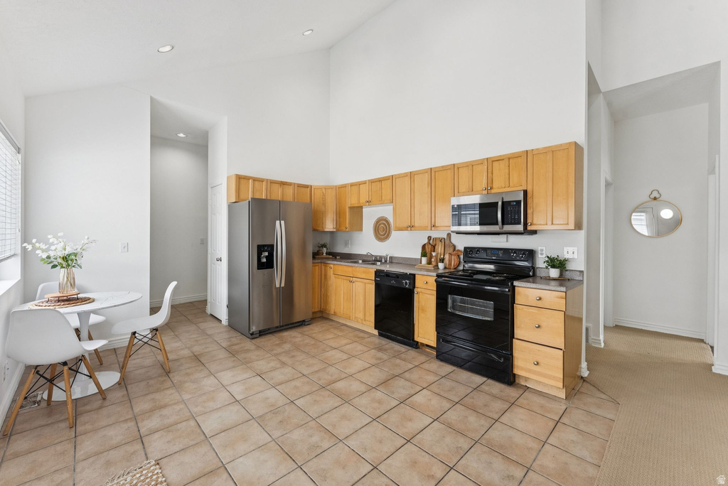 Kitchen featuring black appliances, light tile patterned floors, and vaulted ceiling